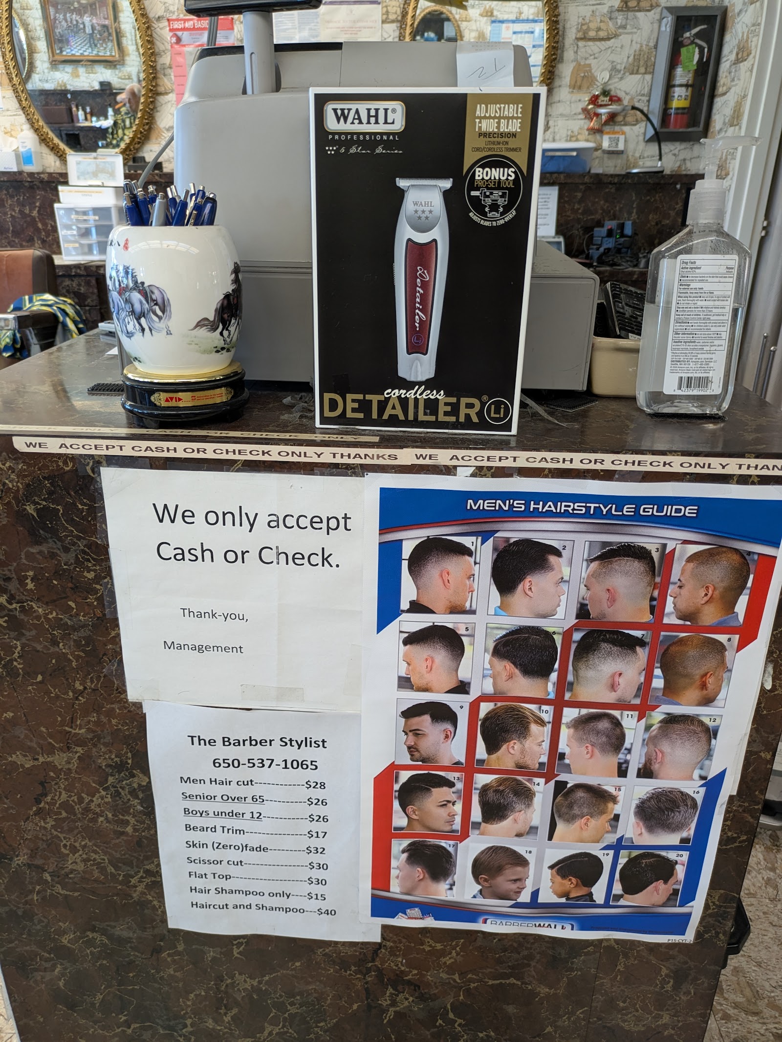 The counter: WAHL clipper display, a hand-printed Cash or Check Only sign, and a men's hairstyle reference poster taped to the mirror.